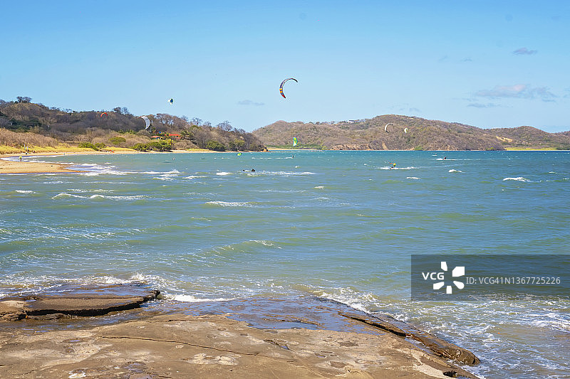 在哥斯达黎加，人们在海上对着山脉和天空玩风筝滑板时看到的海滩景色图片素材