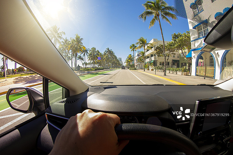 一个年轻的运动男子的视角拍摄在迈阿密海滩艺术装饰区，迈阿密，南佛罗里达，美国，在天堂蓝色的海洋景观前驾驶一辆汽车图片素材