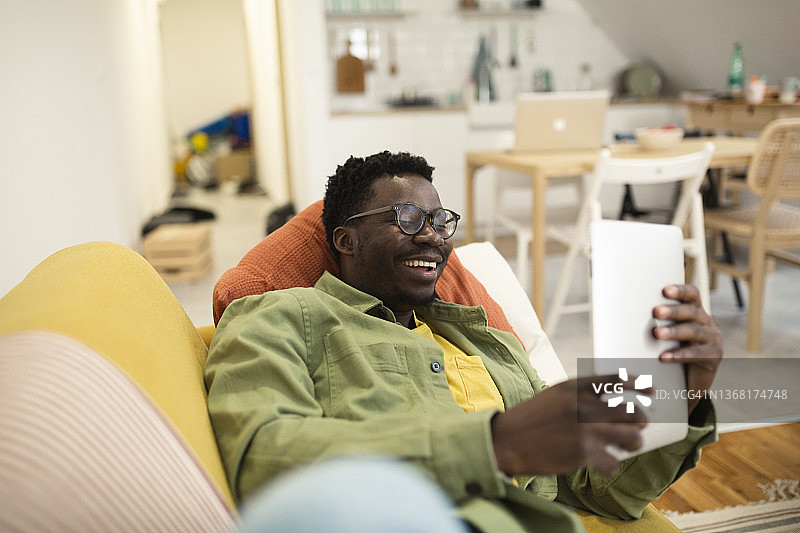 一个快乐的非洲人在沙发上放松和使用平板电脑的肖像图片素材