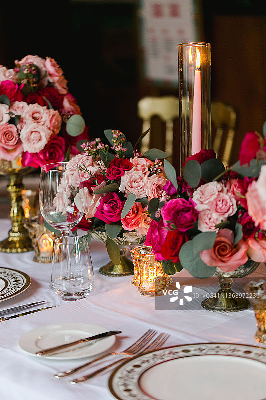 婚礼彩排时，餐桌上摆满了红色和粉色的花束、点燃的蜡烛和祈祷。金盘子、叉子和刀子图片素材