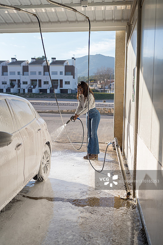 一个女人用高压水射流给他洗车。图片素材