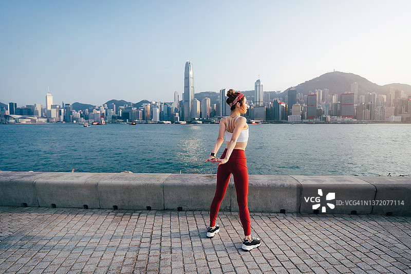 活跃的年轻亚洲运动妇女在运动服装，伸展胳膊和肩膀在户外，站在人行道上壮观的城市天际线在一个阳光明媚的日子。准备锻炼。女孩的力量。健康健身理念图片素材