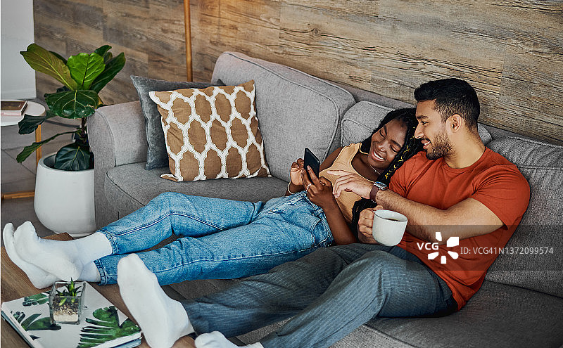 这是一对年轻夫妇躺在家里的沙发上用手机的照片图片素材