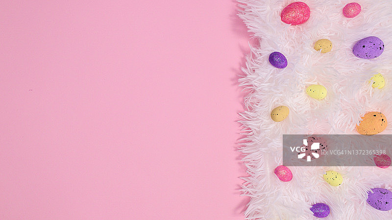 蓬松的白色环保皮毛与彩色鸡蛋在柔和的粉红色背景。创意复制空间平铺图片素材