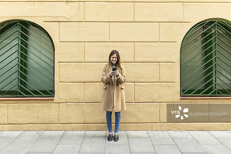 站在墙前的人行道上用智能手机发短信的女人图片素材