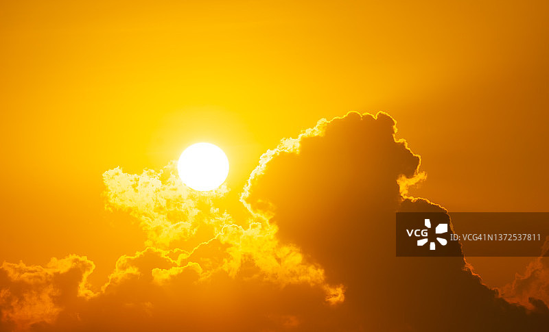 早晨明亮的太阳在云层后面照耀，背景是橘色的天空图片素材