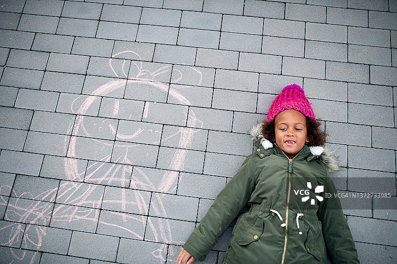 俯视图，小女孩躺在人行道上，旁边是粉笔画。图片素材