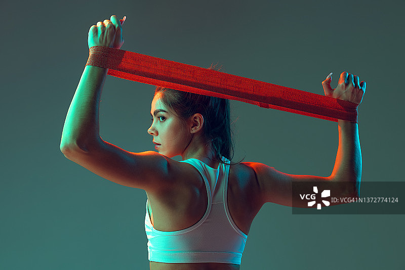 运动的女人锻炼的肖像，做运动设备隔离在绿色工作室背景霓虹灯。运动、行动、健身、青春理念。图片素材