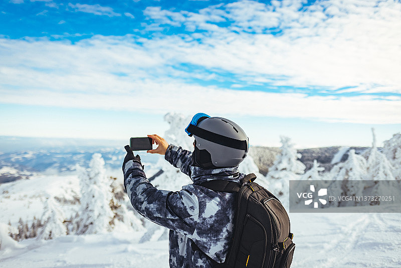 男滑雪者正在拍摄自然的照片，享受冬天的雪山景观。图片素材