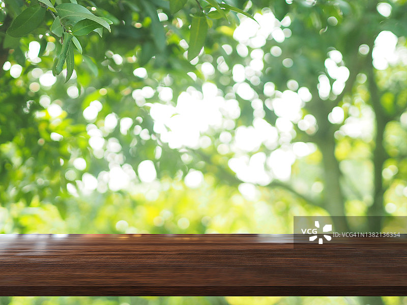 棕色木桌上模糊的绿色自然背景，自然模板绿叶绿叶纹理背光散景阳光展示产品图片素材