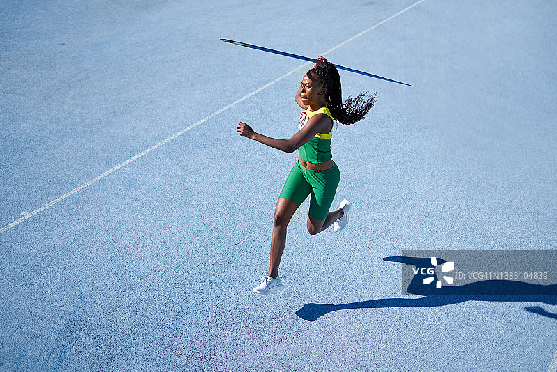 女子田径运动员在阳光明媚的蓝色跑道上投掷标枪图片素材