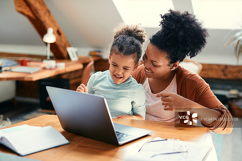 快乐的黑人母亲和女儿在家里使用笔记本电脑玩得很开心。图片素材
