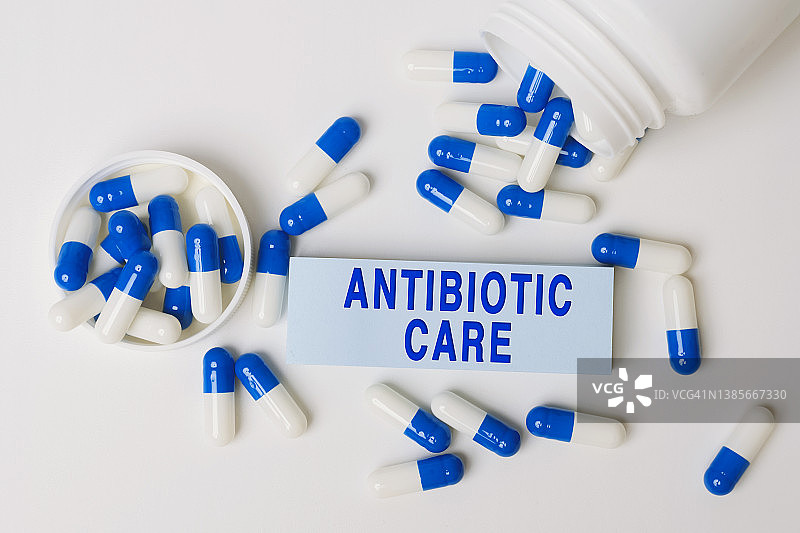 从药瓶里溢出来的蓝白色药丸旁边写着一张纸条，上面写着抗生素护理。医学的概念图片素材