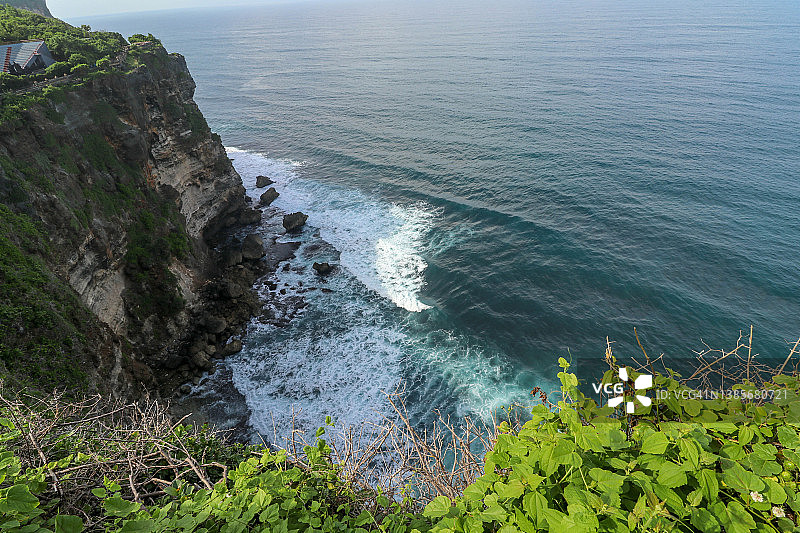 印度尼西亚巴厘岛，乌鲁瓦图悬崖、凉亭和蔚蓝的大海。白天，Pura Luhur Uluwatu寺庙景色优美，前景是五颜六色的花朵。风景优美，海岸景观悬崖高。图片素材