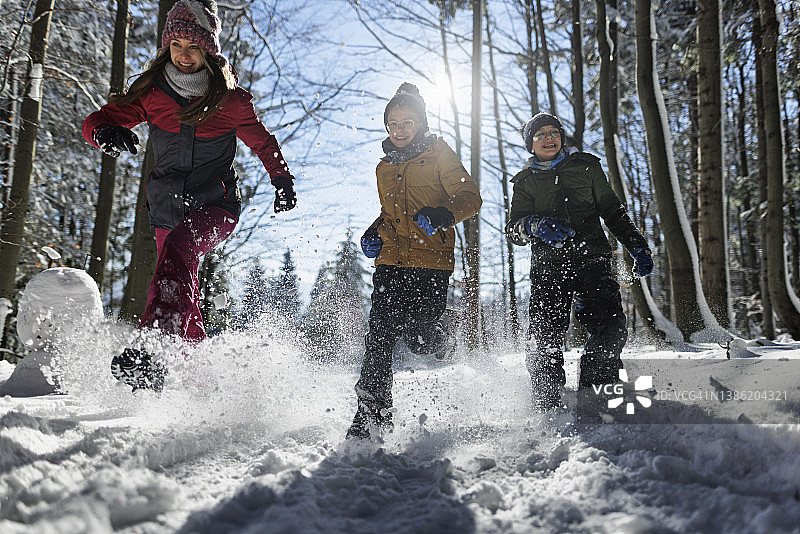 在一个阳光明媚的日子里，快乐的孩子们在美丽的冬季森林里奔跑图片素材