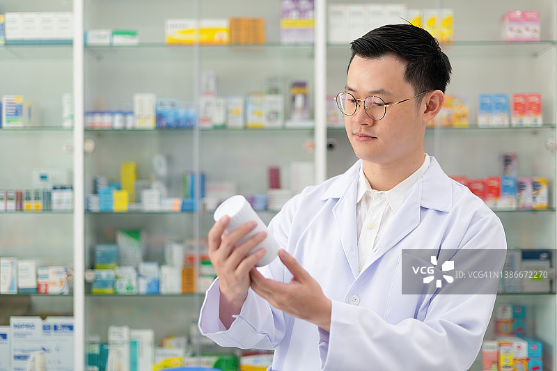 图为，一名年轻的药剂师站在药店的货架前，读着药片的标签，创建药剂师背景。图片素材