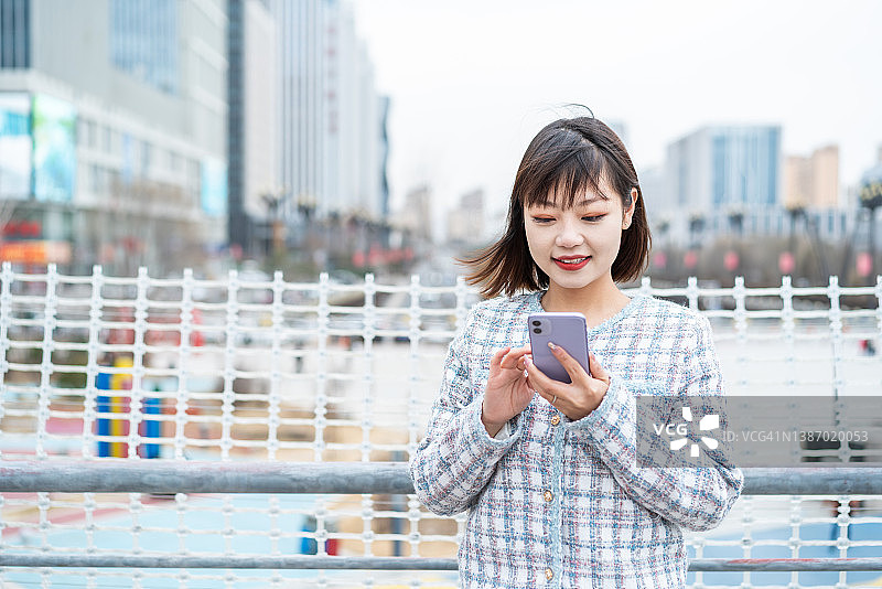 亚洲年轻女子在城市街道上使用智能手机图片素材