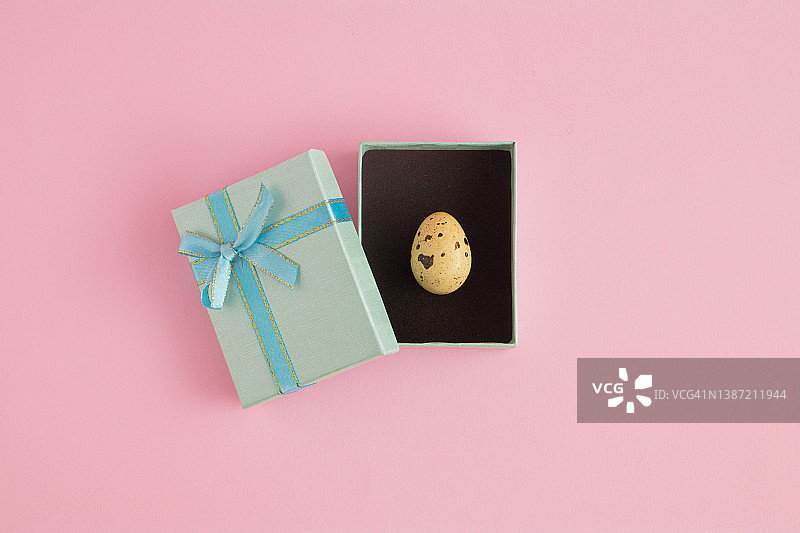 粉红色背景下蓝色礼品盒里的复活节小彩蛋。创意假期或美食概念图片素材