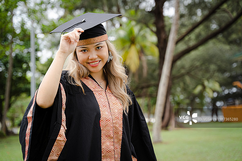 微笑的年轻女子戴着毕业帽和毕业服，骄傲和快乐。图片素材
