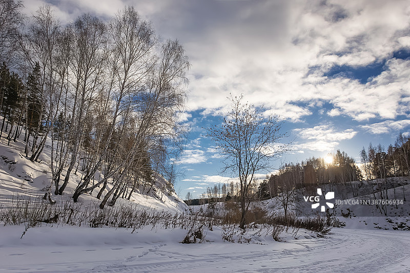 冰冻的河流，风景如画的岩石河岸覆盖着各种植被和雪白的雪。图片素材