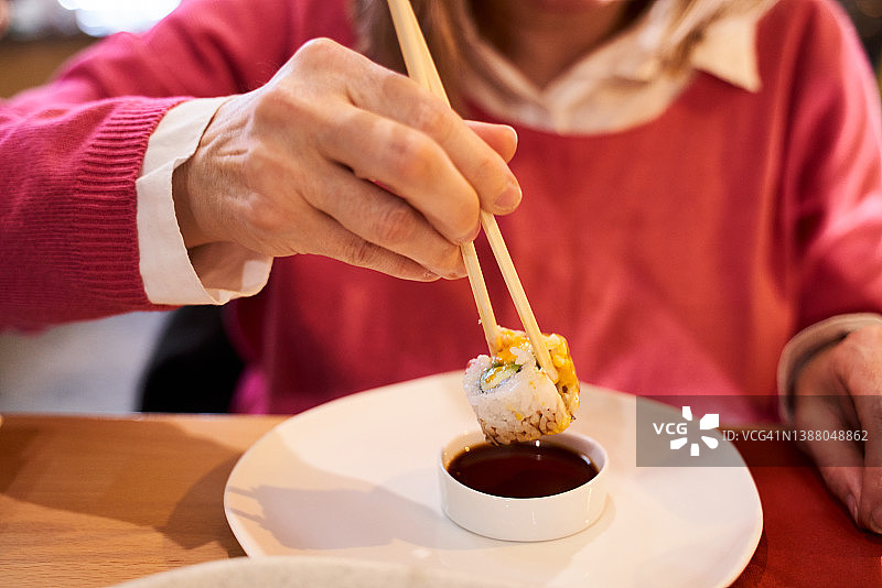 在一家日本餐馆里，白人妇女用筷子夹着蘸着酱油的寿司吃。食品的概念图片素材