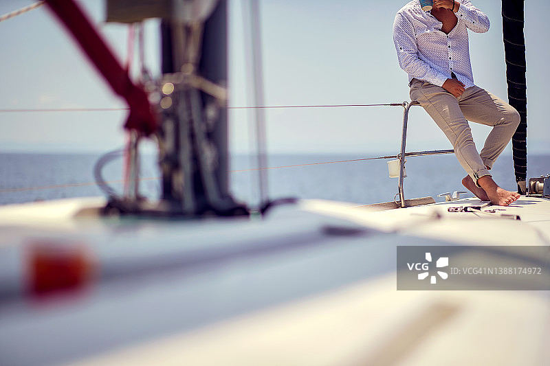 一位年轻英俊的赤脚男模特坐在海边的游艇上，一边喝咖啡，一边享受着拍照的乐趣。夏天,大海,假期图片素材