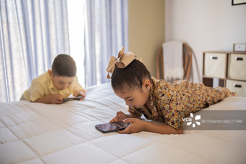 拉丁孩子在家里的床上使用手机图片素材