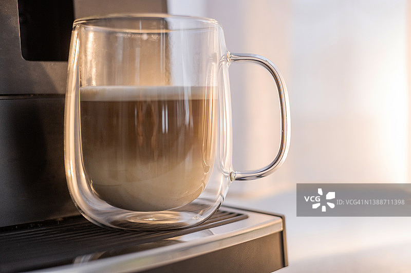 在早晨的阳光下用透明的杯子喝咖啡或卡布奇诺图片素材