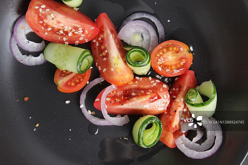 蔬菜沙拉，西红柿，黄瓜，红蓝茄子，白芝麻，在黑色的盘子里，黑色的背景。健康的食物，健康的生活方式图片素材
