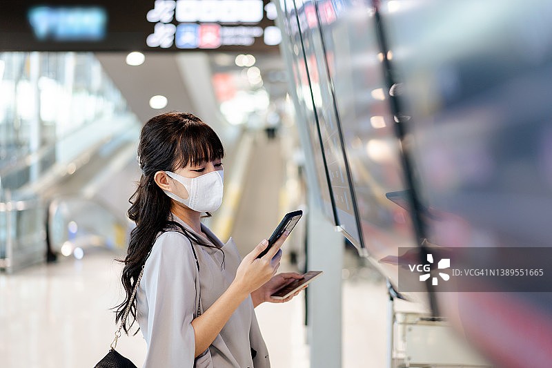 侧面的亚洲年轻女商人检查航班时刻表在机场出发大厅图片素材