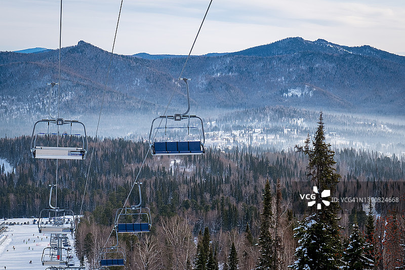 俄罗斯雪列格什滑雪胜地的冬季景观，位于西伯利亚的雪列格什山。滑雪者乘坐的滑雪缆车在高大的冷杉树上滑行图片素材