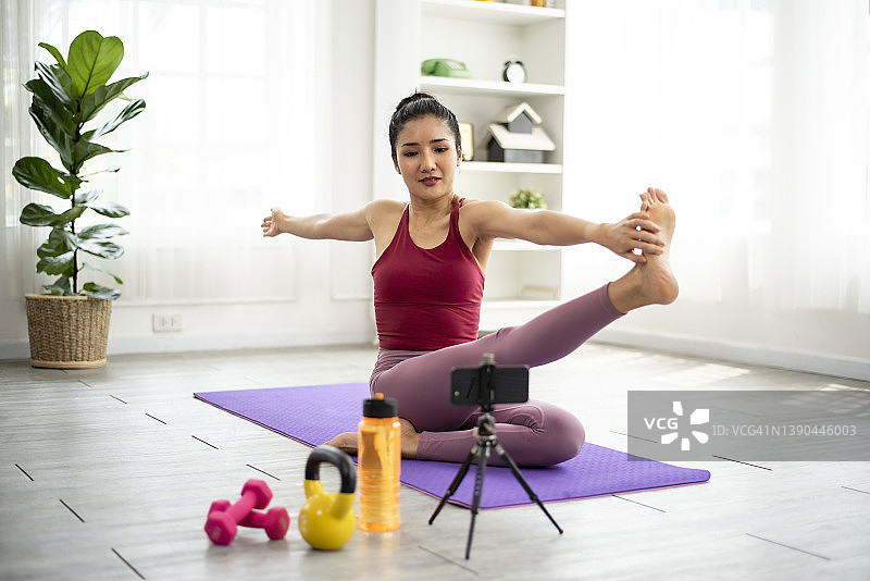 亚洲女性根据在线瑜伽视频在家锻炼。图片素材