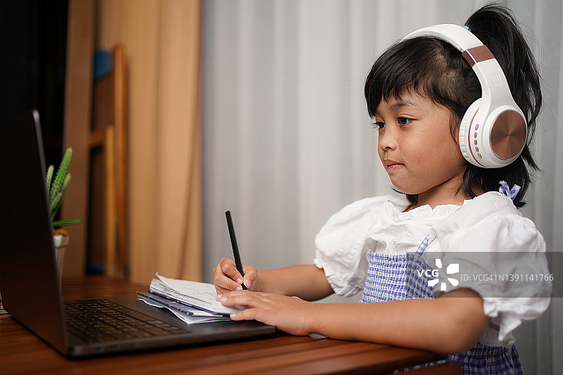 孩子，女孩，学校学生，戴着耳机从家里在线学习，观看网络课程或听老师的视频电话图片素材