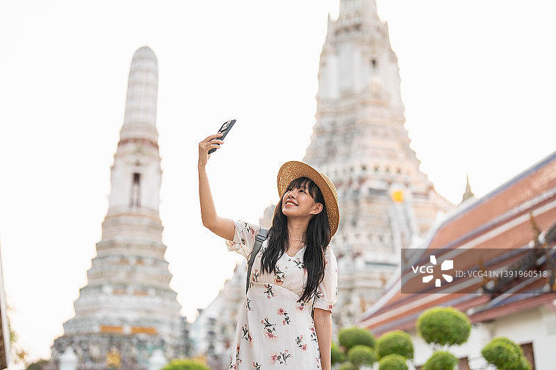 年轻的亚洲女子在曼谷的寺院旅行，用她的智能手机拍照和自拍。图片素材