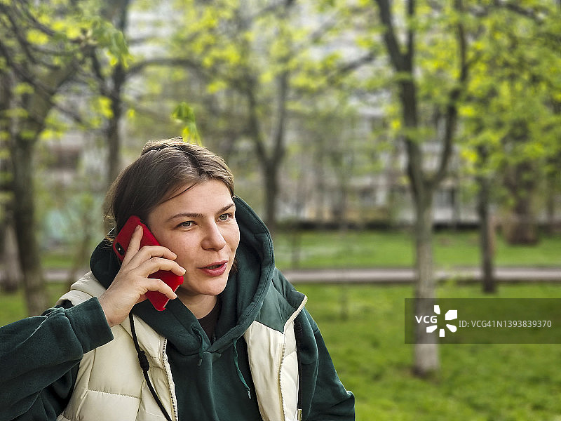在绿色街道背景下用红色电话通话的女人图片素材
