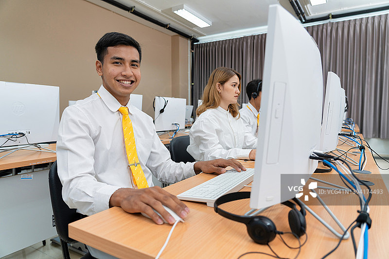 一群亚洲大学生戴着立体声耳机在电脑室学习图片素材