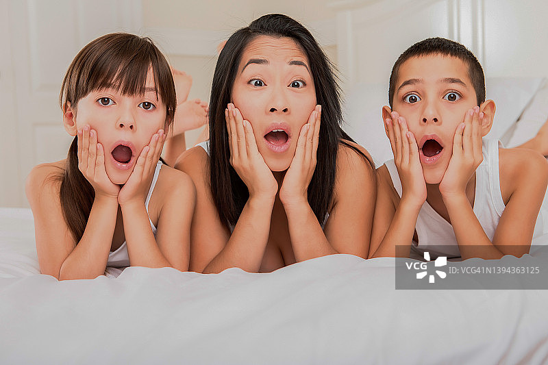 震惊的妈妈和两个孩子躺在床上图片素材