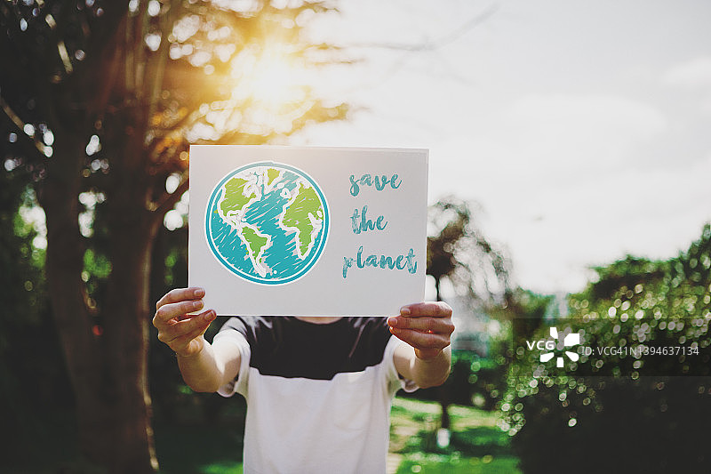 小男孩举着一个纸板牌子，上面写着“拯救地球”。图片素材