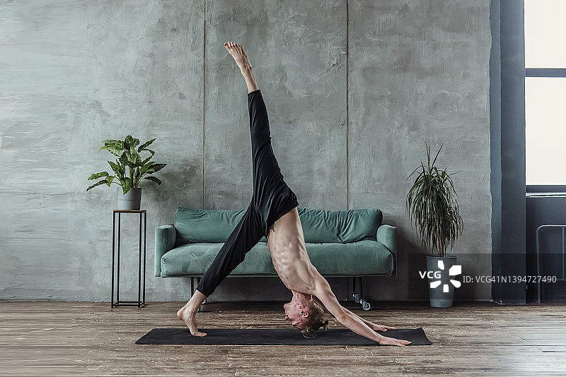 一名男子在家里客厅的地毯上练习瑜伽。早晨体操锻炼图片素材