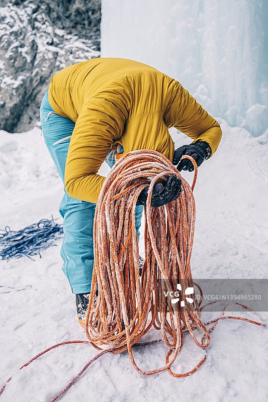 在加拿大落基山脉，一名妇女在冰上攀爬时从肩上取下一根卷绳子图片素材