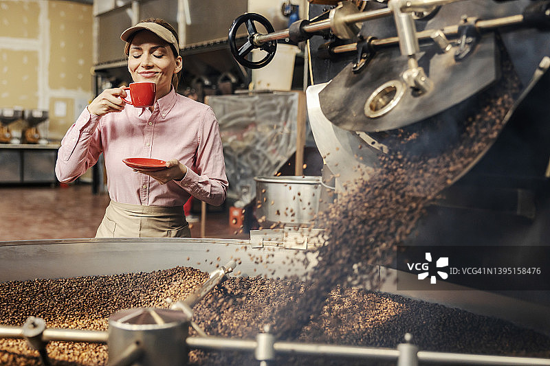 一位快乐的女工站在烘咖啡机旁闻着新鲜的咖啡。图片素材