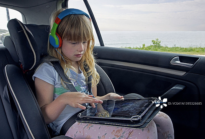 儿童(6-7岁)在车内戴着耳机玩平板电脑图片素材