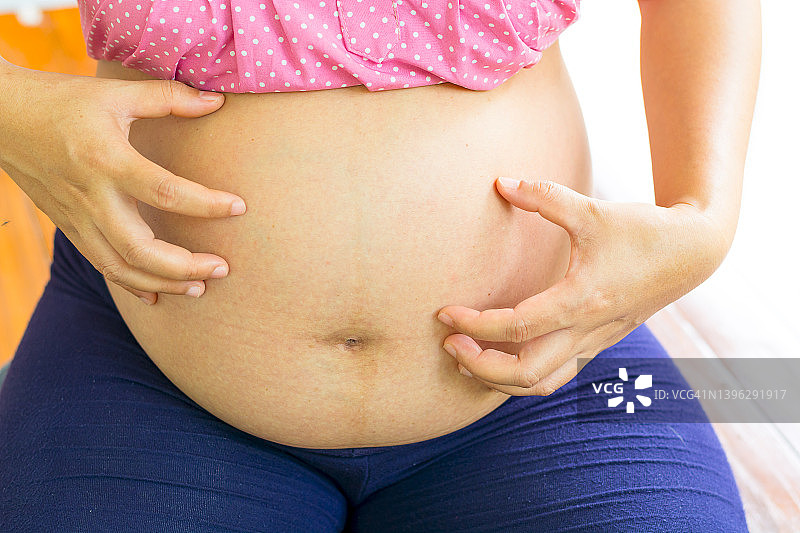 孕妇在衣服上手拉手在肚子上的背景怀孕，孕妇准备和期待的特写拷贝空间图像怀孕的温柔的情绪。图片素材