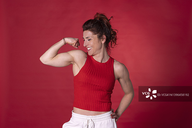 微笑的女人在红色背景下展示肌肉图片素材