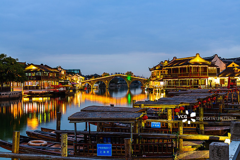 上海朱家角古镇。沿河的房屋灯火通明以吸引游客。游船停泊在码头。图片素材