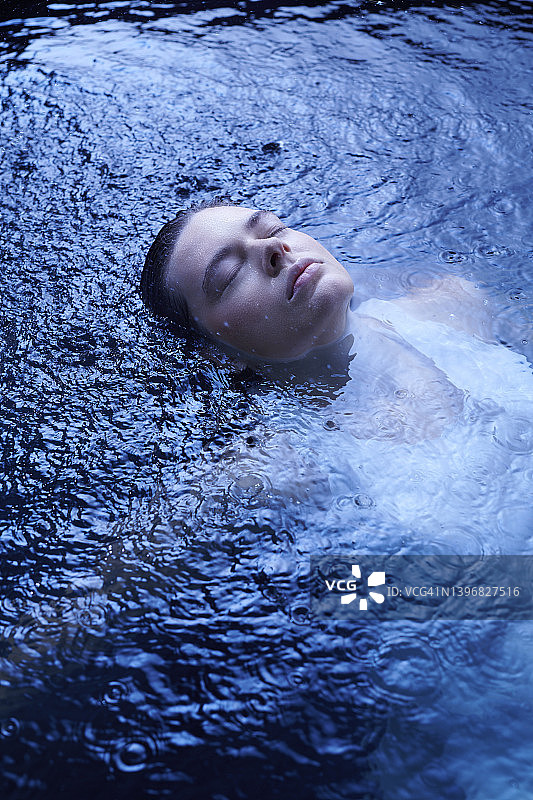 一个娇嫩的女人漂浮在清澈湛蓝的水面上。享受精致的波。自然美容护理隐喻图片素材