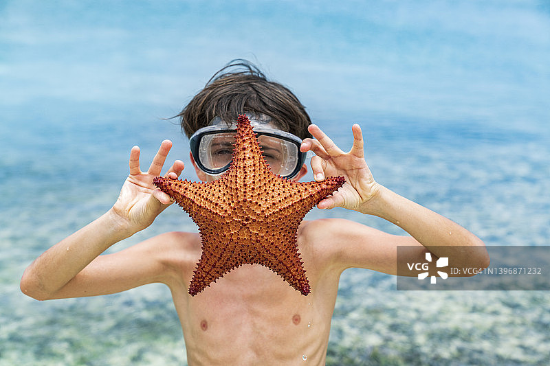 快乐的小男孩戴着潜水面具，手里拿着一只海星图片素材