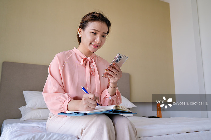 年轻的亚洲女性在家工作时使用智能手机图片素材