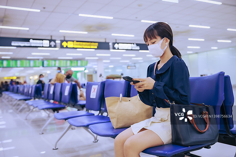 年轻的亚洲女企业家戴着口罩，在机场出境区用手机阅读电子邮件。商务旅行的概念。图片素材