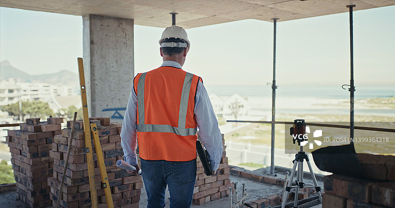 检查建筑工地的建筑承包商在一个建筑项目中，一个男人走过一栋建筑的后视图图片素材